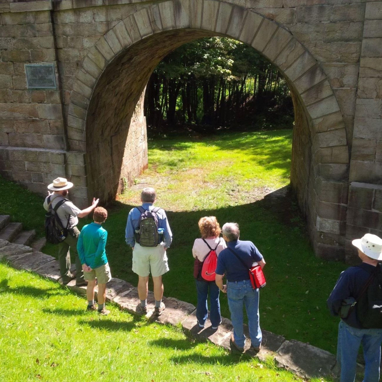 A park ranger in uniform talking in front of a 19th century bridge