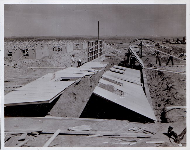 A barrack being constructed. The walls are lying on the ground and other partly constructed barracks are visible in the background.