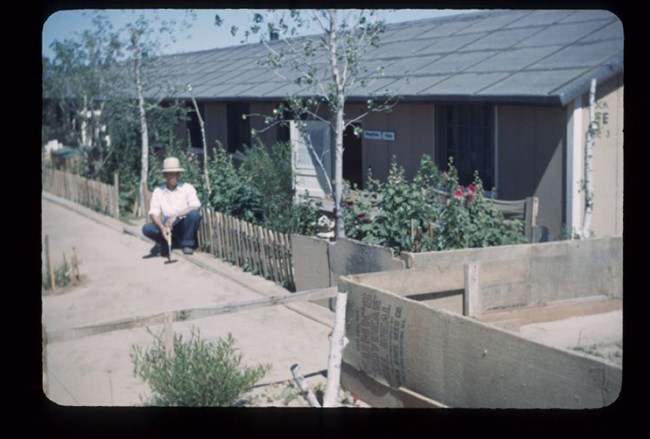 A man kneels next to a garden behind a barrack