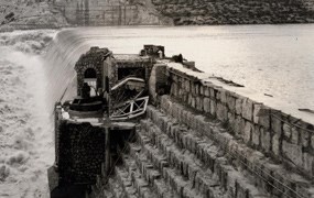 Black and white photo showing large amounts of water flowing over spillway of dam