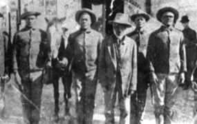 Six black men in Union uniforms with 4 men standing at attention and one horse posing in front of an encampment.