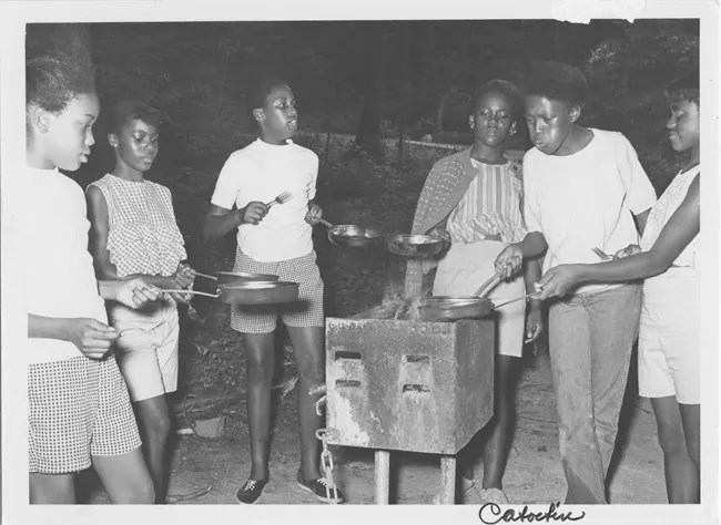 Six young children are standing around a grill with pots in their hands