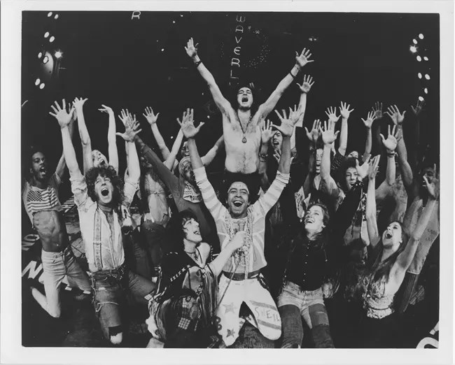 A large group of people raise their hands in the air in happiness.