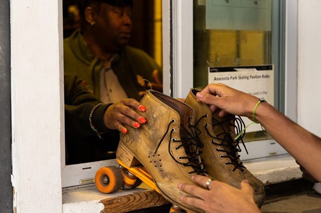 A visitor is handed a pair of rental skates by a park ranger.