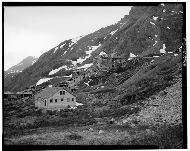 Black and white; a few buildings, mountainside with snow.