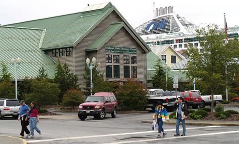 Green roofed building with cruise ship in background and people walking in front.