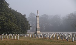 A tall monument topped by a soldier statue is surrounded by graves.