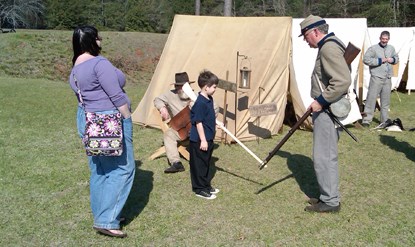 A boy with a wooden musket practices rifle drill with a Civil War soldier.