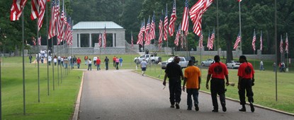 Men walk down a cemetery avenue lined with American flags