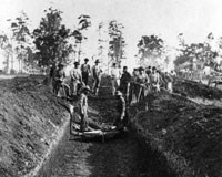Men standing in a waist-deep burial trench