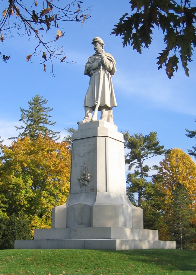 A stone statue of a Civil War soldier leaning on a rifle atop a stone plinth.