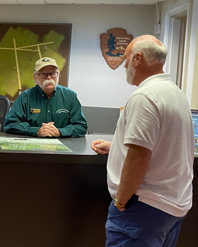 A park volunteer in uniform in conversation with a visitor