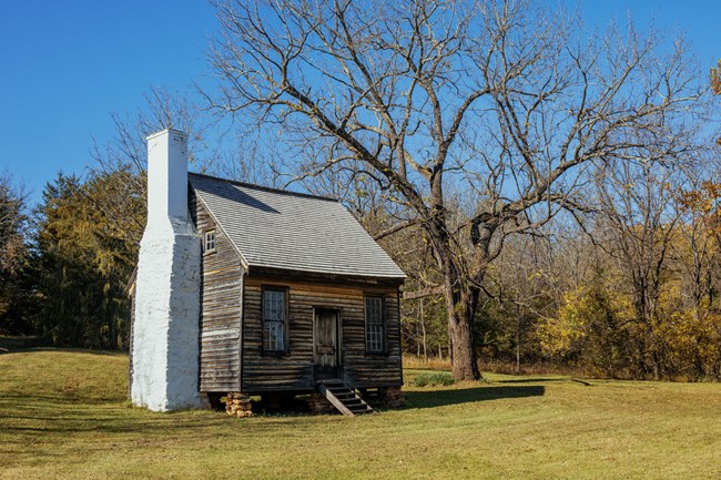 A small 1830s wooden cabin with a stone chimney