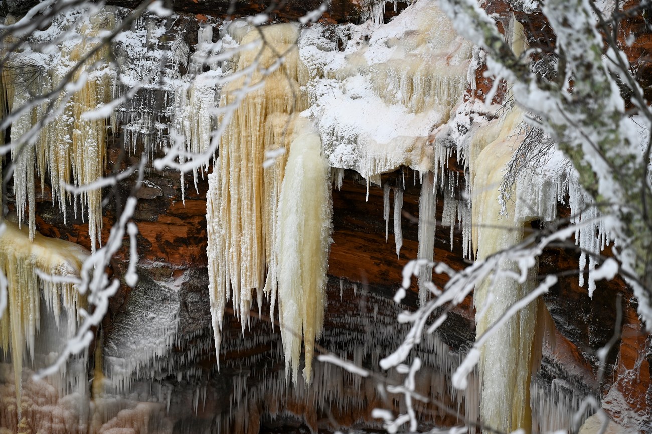 Red sandstone cliffs draped in icicles and ice columns of various sizes.