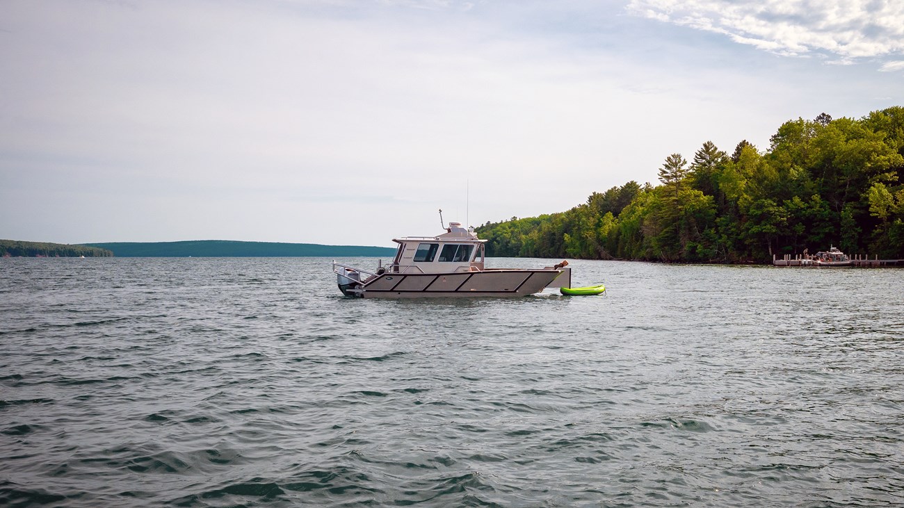 Photograph of grey metal boat on lake with a tree lined shore visible in the background.