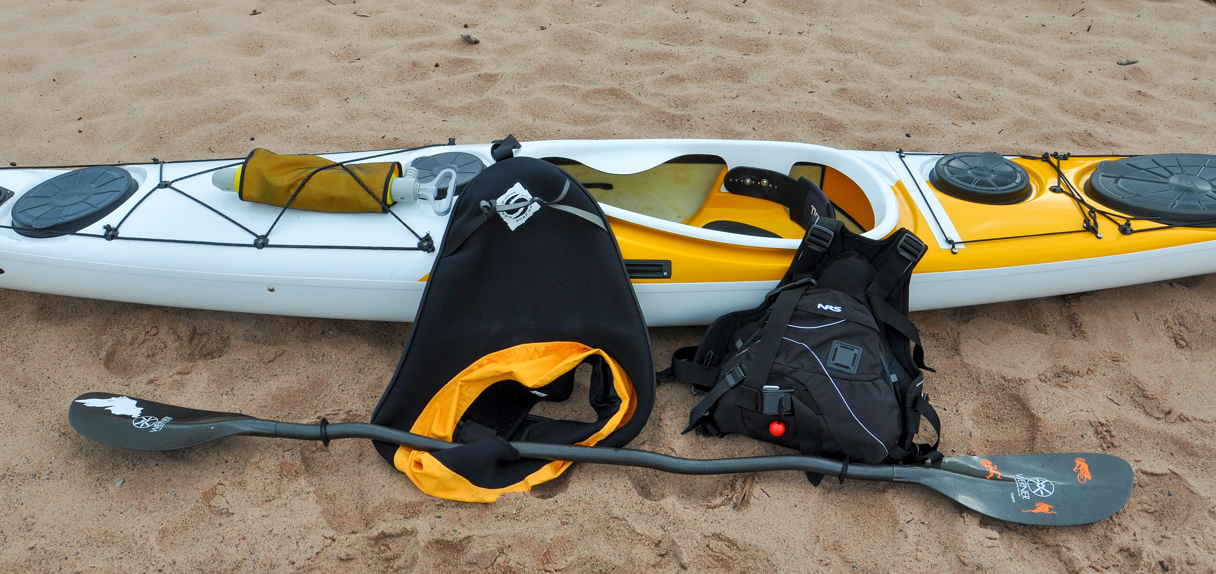 Photograph of kayak and kayaking equipment on sandy beach.