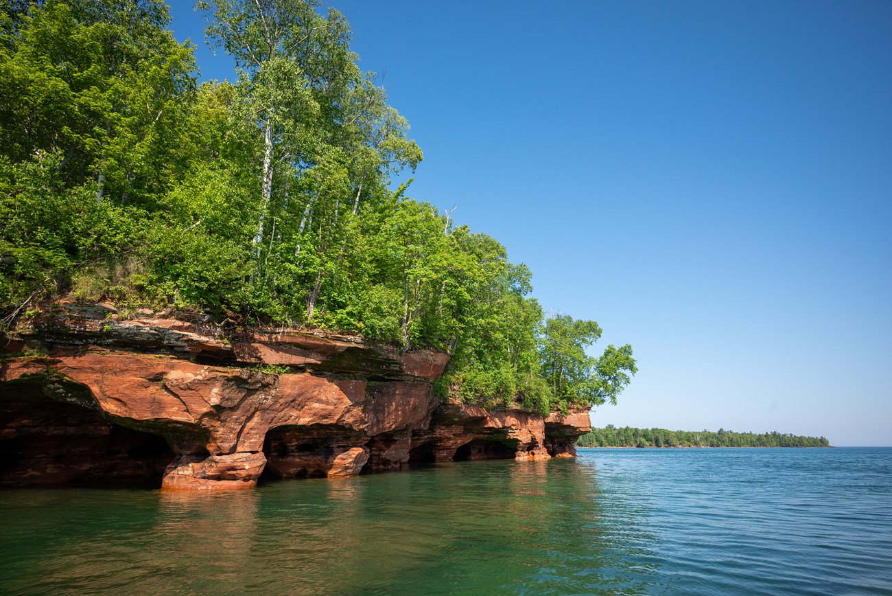 Photograph of sandstone sea caves and blue-green lake water.