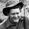 A black and white photo of a young man wearing a jacket and a hat smiling at the camera.