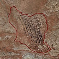 A satellite image of a red desert landscape. The center of the image contains dozens of rocky fins running parallel to one another. A red line is drawn around the area containing the rocky fins.