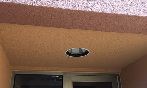 A recessed light fixture in the ceiling of an outdoor alcove above a door.