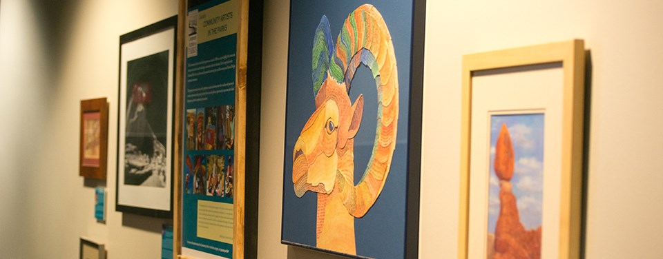 Artwork of a bighorn sheep hanging on a wall surrounded by paintings and photographs that are out of focus.