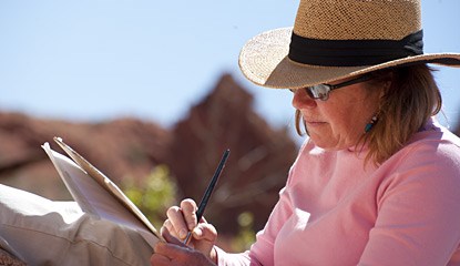 a woman wearing a pink shirt and straw hat holds a paintbrush.