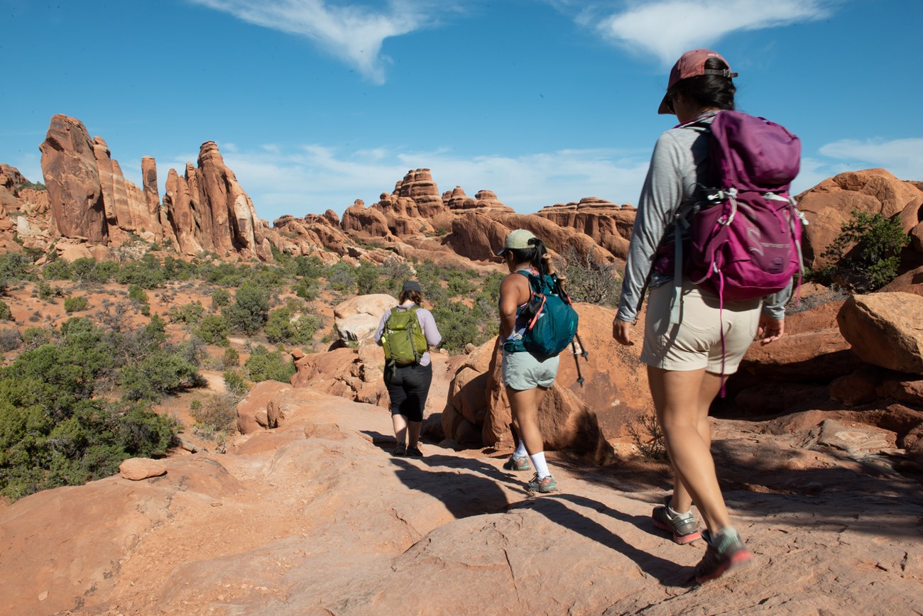 Three hikers in colorful gear traverse a trail in Arches.