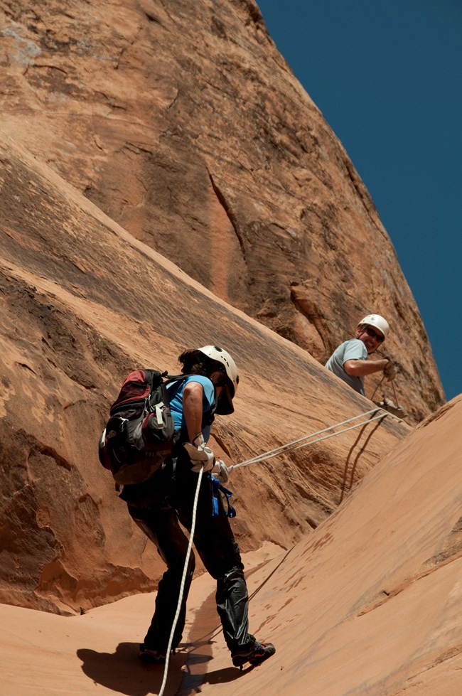 A woman descends a steep canyon wall using ropes during a canyoneering expedition.