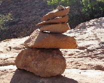 A stack of 5 orange colored rocks in various sizes. The stack creates a half a foot pile and sits on exposed hard rock.