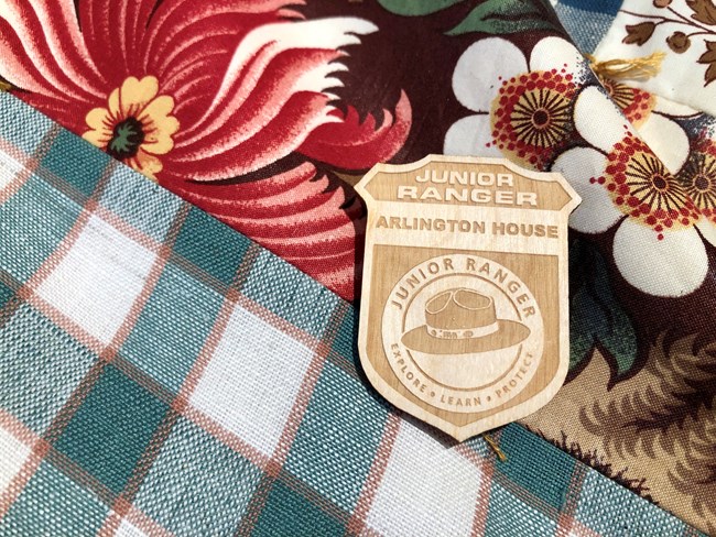 A children's wooden park ranger badge resting on plaid and floral fabric