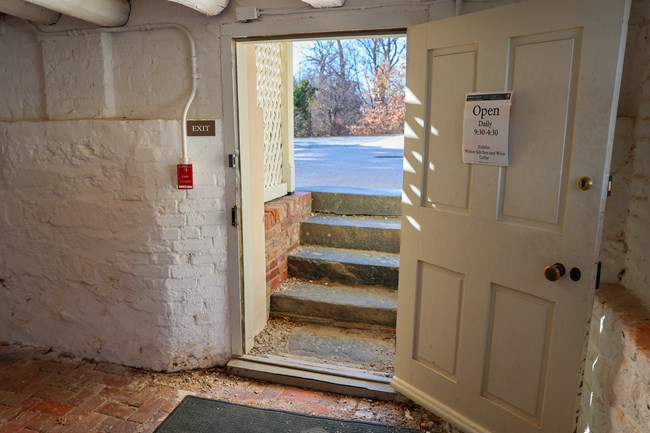Four steps leading up out of a basement and outside through an open door.