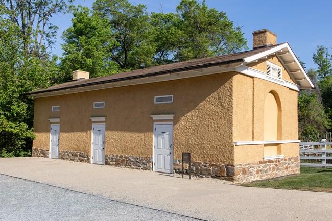 A single-story rectangular building with three white doors and a paved sidewalk.