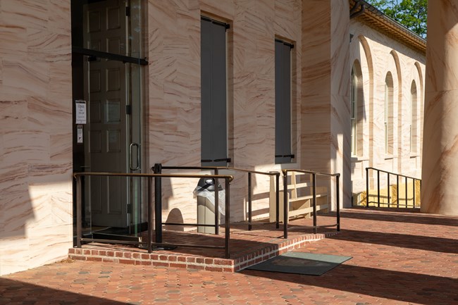 A set of two ramps with railings lead up to a brick porch and up to an open glass door.