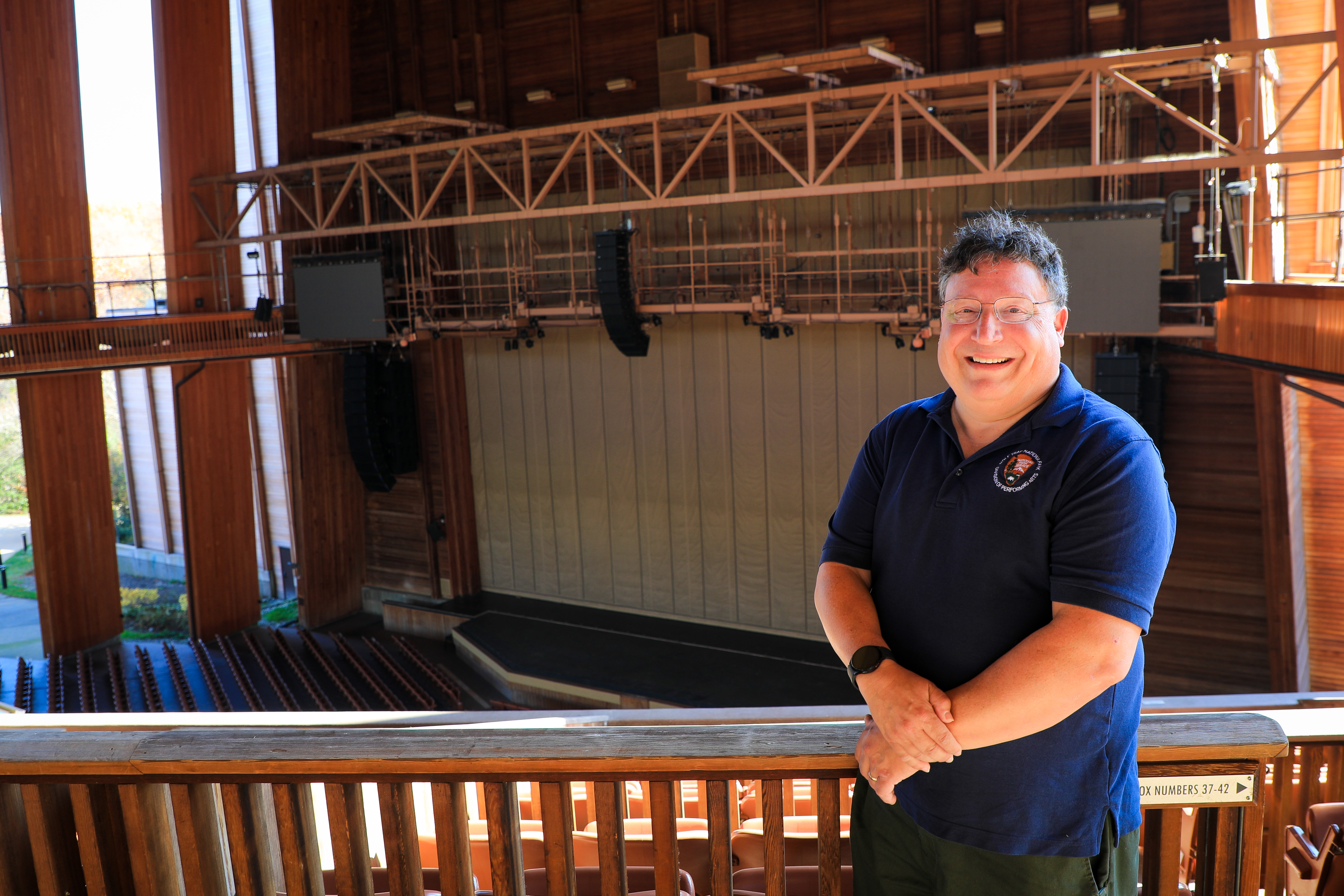 A white male poses by box seats in a wooden amphitheater.