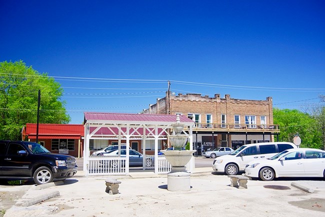 Street scene with vehicles in front of a brown masonry building and a red building
