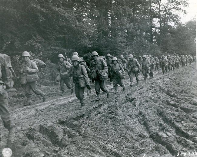 Men in military uniforms marching down a muddy road