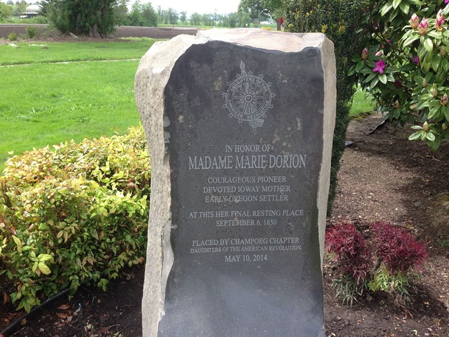 A large vertical stone, with a commemorative metal plate attached to the front, which reads, “In honor of Madame Marie Dorion, courageous pioneer, devoted Ioway mother, early Oregon settler, at this her final resting place, September 6, 1850.  Placed by C