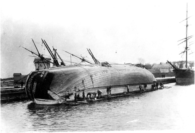 a ship careened on its side with workers cleaning the bottom