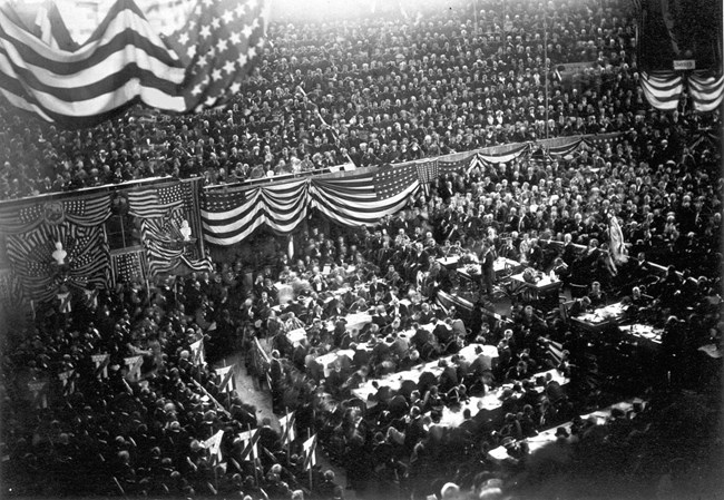 a large group of men who are both sitting and standing inside a large hall