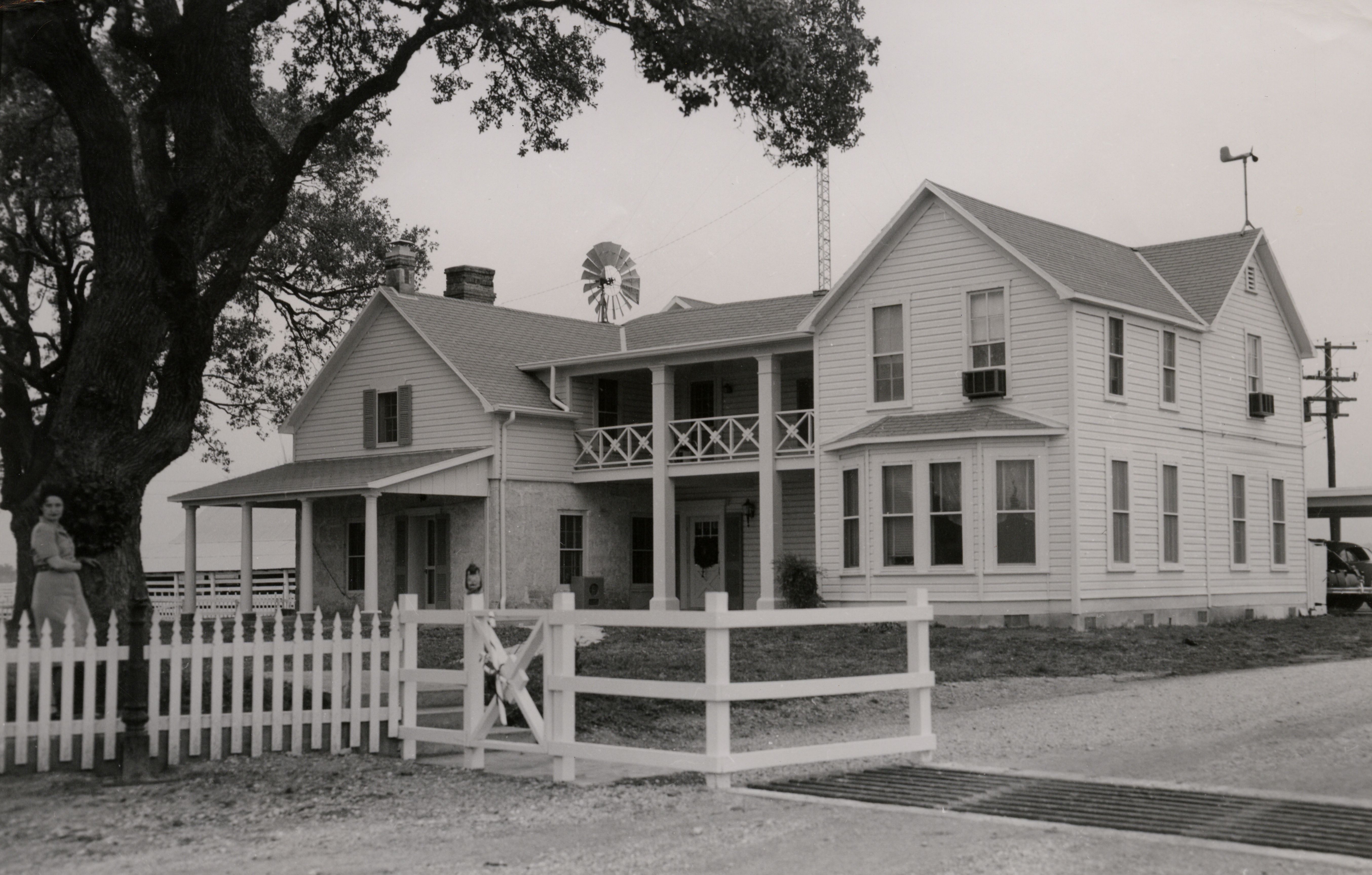 Lady Bird Johnson leans against a tree in the yard of a two-story frame house