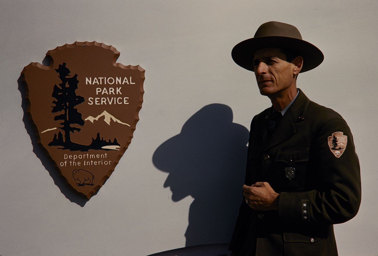 Man in ranger uniform stands in front of a wall looking at an arrowhead plaque.