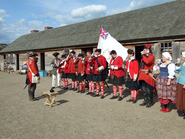 Men in bright red jackets and tartan kilts stand shoulder to shoulder.