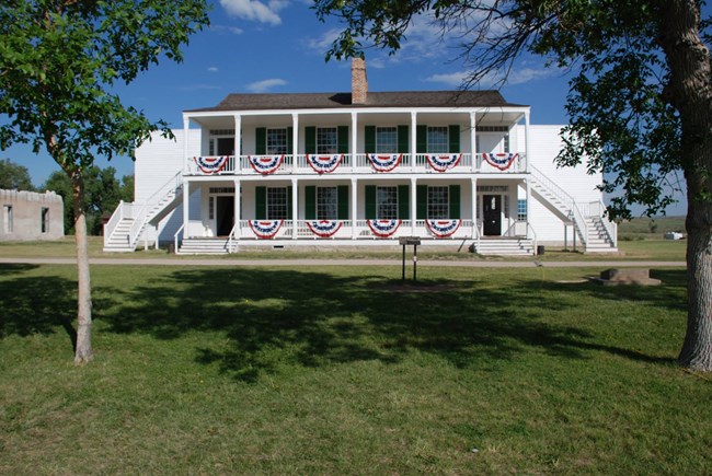 A two story, wood-sided building is painted white with a large porch on the front.