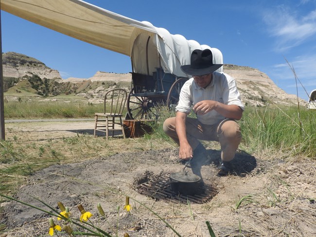 A man dressed in period clothing tends to a ground fire.