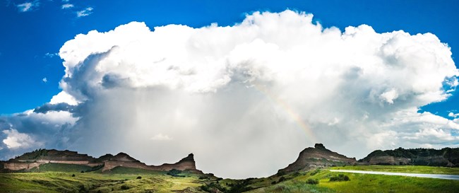 Storm clouds gather over a pass between two sandstone bluffs.