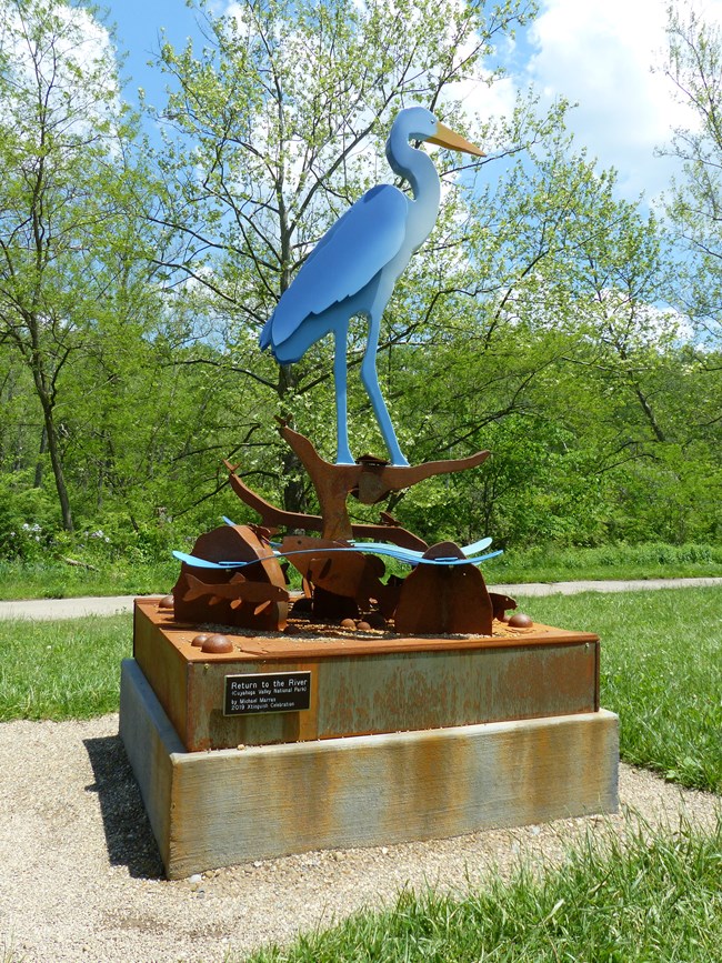 A metal statue of a blue-and-white heron standing in water.