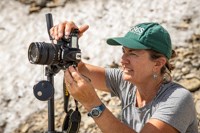 A person in a green USGS hat uses a camera.