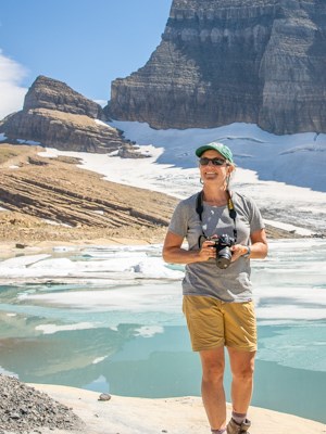 A person smiling in front of an icy lake holding a camera