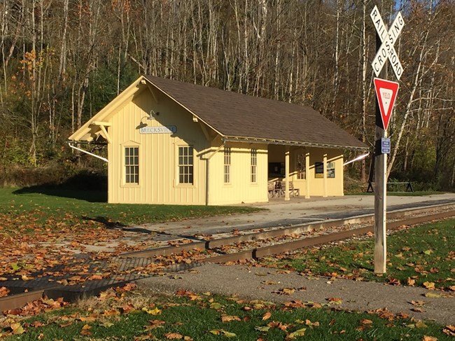 A yellow building beside railroad tracks with a railroad crossing sign to the right.