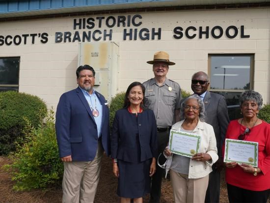 Three women and three men standing in front of a school